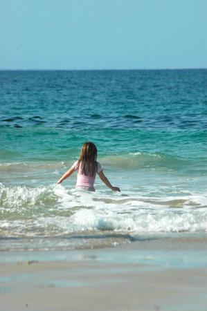Backview of a caucasian white girl child with long blond hair standing and playing in the water of the Indian ocean on a beach in South Africa during summer holidaysの写真素材