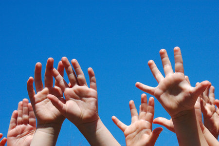 Lots of little hands of caucasian white children raising up their arms into the blue sky outdoors の写真素材