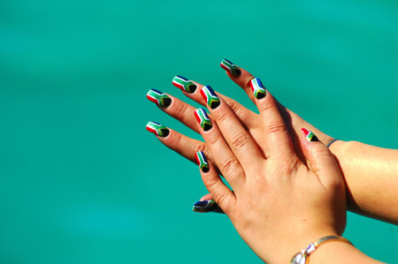 The caucasian white hands of a female South African Rugby supporter in front of blue background. Her finger nails are painted in the colors of the national flag of the Rainbow Nation, South Africa, by a professional nail technicianの写真素材