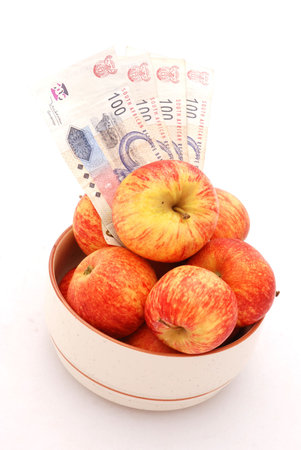 A big bowl full of red apples and four one hundred Rand bills of South African money. Image isolated on white backgroundの写真素材