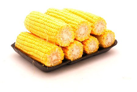 Seven delicious cooked corn cobs on a black board isolated on white backgroundの写真素材