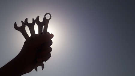A worker is holding wrench in his hand tightly in front of the sun in blue sky, labours day or workers dayの写真素材