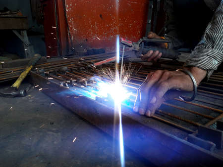 Generating blue sparks while worker welding on iron in industrial workshop related to construction