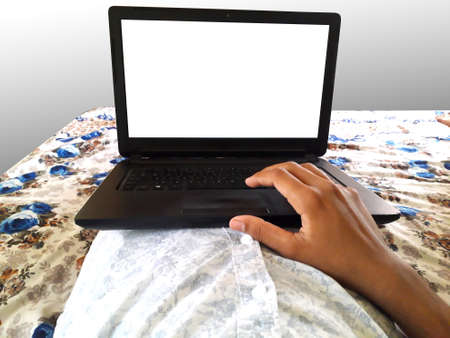 a male doing work on black laptop lying down on bed white screen mockup work from home in lockdownの写真素材