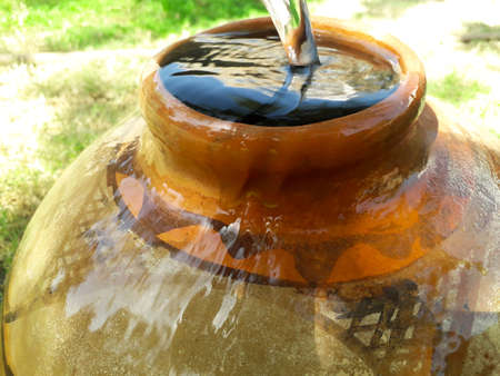 Filling water in a clay pot in summer during lack of water in rural areas and water is overflowingの写真素材
