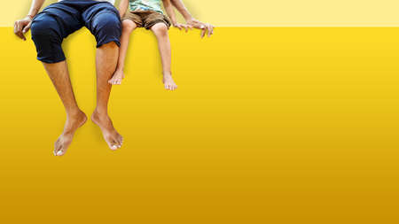 Father and daughter sitting on yellow color wall and hanging feet outdoor .