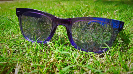 Blue transparent sun glasses or specs placed on green grass or weed surface in a gardenの写真素材