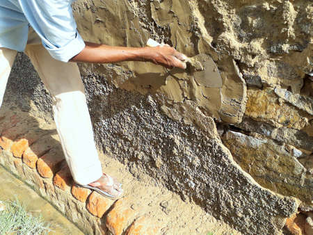 mason repairing damaged wall with paste of cement on a siteの写真素材