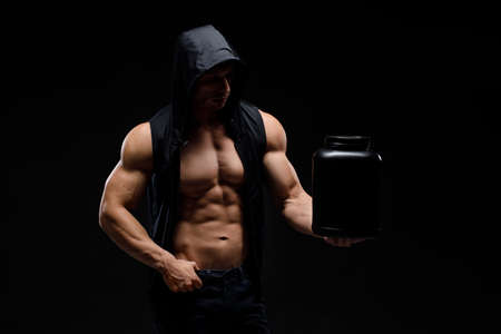 Muscular bodybuilder with jar of protein on a black background. Sports nutrition. Bodybuilding nutrition supplements, workout, healthy lifestyle concept.の写真素材