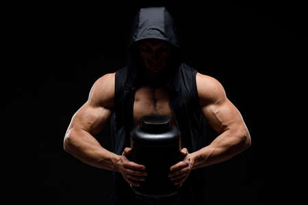Muscular bodybuilder with jar of protein on a black background. Sports nutrition. Bodybuilding...