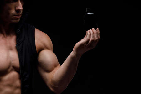 Muscular bodybuilder with jar of protein on a black background. Sports nutrition. Bodybuilding...