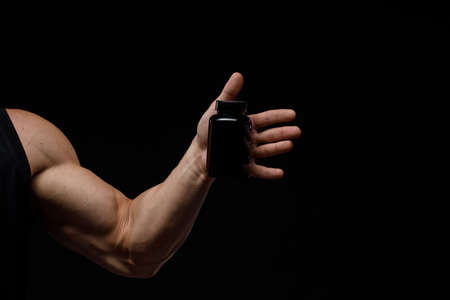 Muscular bodybuilder with jar of protein on a black background. Sports nutrition. Bodybuilding nutrition supplements, workout, healthy lifestyle concept.の写真素材
