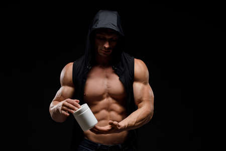 Muscular bodybuilder with jar of protein on a black background. Sports nutrition. Bodybuilding nutrition supplements, workout, healthy lifestyle concept.の写真素材