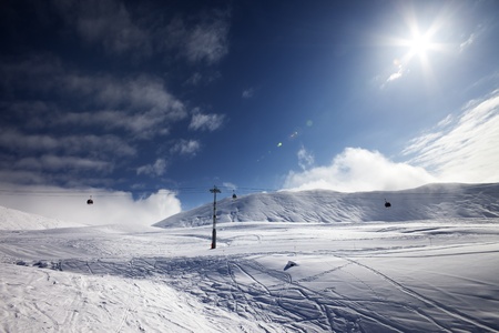 Ski slope, gondola lift and blue sky with sun. Georgia, ski resort Gudauri. Caucasus Mountains