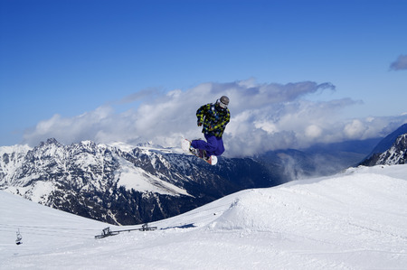 Snowboarder jumping in terrain park at snow mountain on sunny winter day. Caucasus Mountains, region Dombay.の写真素材