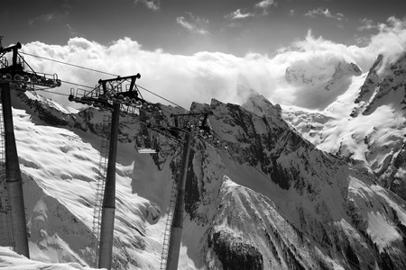 Black and white view on cable car at ski resort and mountains in sunlight clouds. Caucasus Mountains, region Dombay.の写真素材