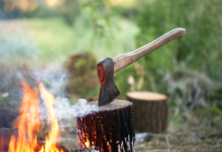 Axe in tree stump and campfire with smoke in summer forest at sun eveningの写真素材