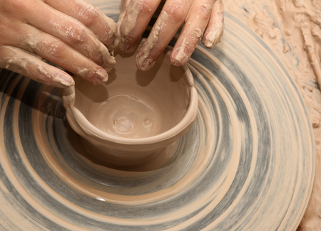 Woman in process of making clay bowl on pottery wheel. Potter at work. Close-up view.