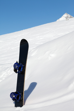 Snowboard in snowdrift after snowfall and mountains in background at nice sun day. Caucasus Mountains in winter, Georgia, region Gudauri.の写真素材
