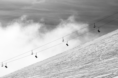 Snowy off-piste ski slope and silhouette of chair-lift in fog. Caucasus Mountains in winter, Georgia, region Gudauri. Black and white toned image.

の写真素材