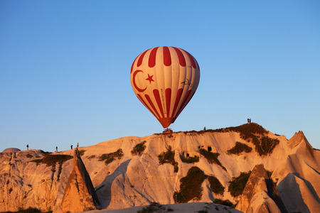 GOREM, CAPPADOCIA,TURKEY - MAY 07, 2013: Hot air balloon with Turkish symbolic on blue clear sunlight sky and fairy chimneys rock formations at sunriseのeditorial素材