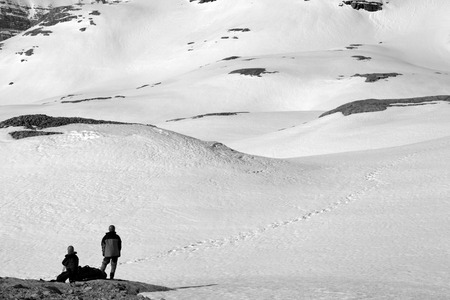 Two hikers on halt in snowy mountain. Black and white toned landscape.のeditorial素材