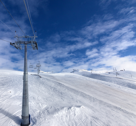 Snowy ski slope, chair-lift on ski resort and blue sky with clouds at windy day. Caucasus Mountains in winter, Georgia, region Gudauri.の写真素材