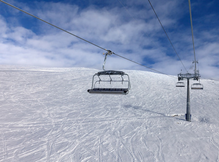 Snowy off-piste ski slope, chair-lift on ski resort and blue sky with clouds. Caucasus Mountains in winter, Georgia, region Gudauri.の写真素材