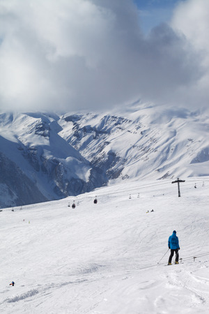 Skier descend on snowy ski slope and gondola lift at sun cloudy day. Georgia, region Gudauri. Caucasus Mountains in winter.の写真素材