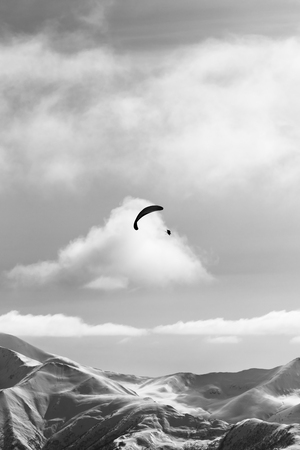 Silhouette of paraglider in winter snowy mountains at nice sun evening. Caucasus Mountains, Georgia, region Gudauri. Black and white toned landscape.の写真素材