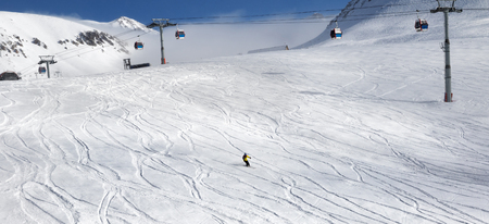 Skiers downhill on ski slope with trace from skis and snowboards and gondola lift at nice sun day. Georgia, region Gudauri. Caucasus Mountains in winter. Panoramic view.の写真素材