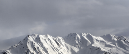 Panoramic view on evening snowy sunlight mountains and gray sky. Caucasus Mountains in winter....