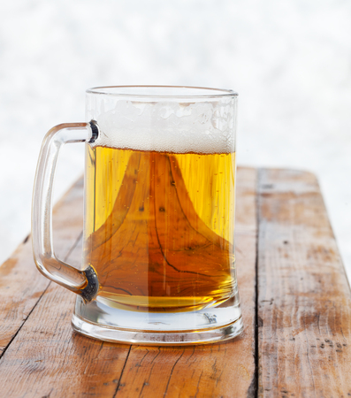 Glass mug with fresh beer on wooden bench in winter outdoor cafe at ski resortの写真素材