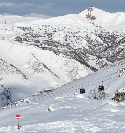 Snow-covered ski slope in snowy mountains and gondola lift. Caucasus Mountains at sunny winter day, Shahdagh, Azerbaijan.の写真素材