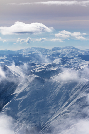Snowy sunlight mountains in haze and multicolor cloudy sky. Caucasus Mountains, Georgia, region Gudauri at winter.の写真素材
