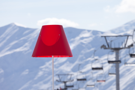 Lamp with red lampshade in outdoor cafe at ski resort, snowy winter mountains and chair lift in background. Caucasus Mountains. Georgia, region Gudauri.の写真素材