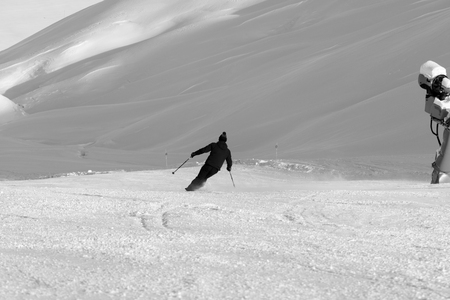 Skier downhill on prepared snowy ski slope with snow cannon at sun winter day. Caucasus Mountains, Shahdagh, Azerbaijan. Black and white toned landscape.の写真素材