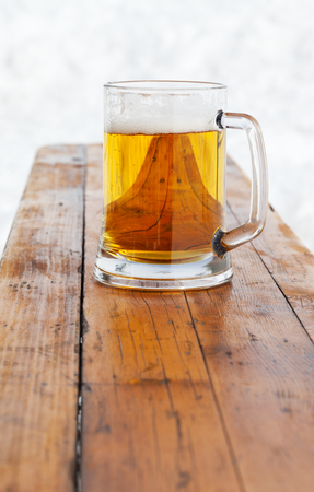 Glass mug with fresh cold beer on wooden bench in winter outdoor cafe at ski resortの写真素材