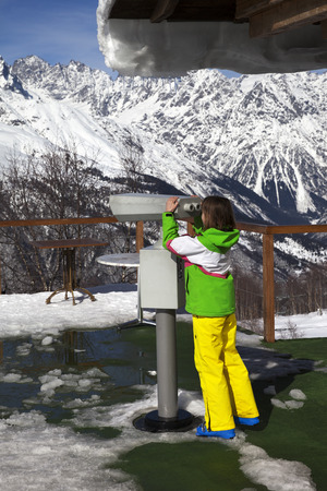 Girl skier looks through binoculars on observation deck of ski resort in winter mountain at sunny day. Caucasus Mountains. Hatsvali, Svaneti region of Georgia.の写真素材