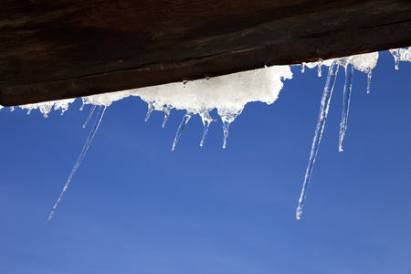Wooden roof with snow cornice and icicles at sun winter day. Bottom view. Selective focus.の写真素材