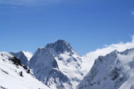Winter snowy mountains in clouds and beautiful blue sky at sunny day. Caucasus Mountains, region Dombay.の写真素材