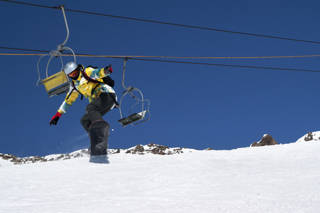 Snowboarder jumping on snowy ski slope, chair lift and blue clear sky at background. Caucasus Mountains in sunny winter day, region Dombay.の写真素材