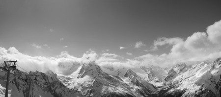 Black and white panorama of snowy sunlight mountains in clouds and chair-lift at sun winter day. Caucasus Mountains, region Dombay.

の写真素材