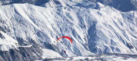 Panoramic view on paragliding at snowy mountains over ski resort at sunny winter day. Caucasus Mountains. Georgia, region Gudauri.の写真素材