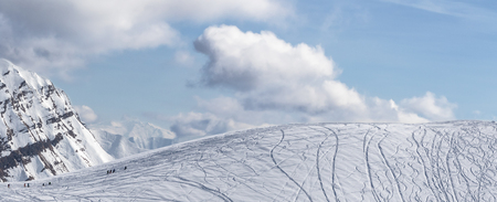 Panoramic view on snowy off piste slope for freeriding with traces from skis, snowboards and silhouette of freeriders at sunny winter day. Caucasus Mountains, Georgia, region Gudauri.の写真素材