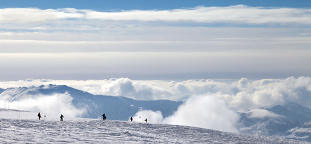 Panoramic view on silhouettes of skiers and snowboarders on snowy ski slope and mountains in beautiful clouds at winter evening. Caucasus Mountains, Georgia, region Gudauri.の写真素材