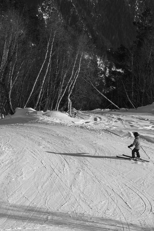 Skier descent on snowy ski slope in forest at sun winter day. Caucasus Mountains. Hatsvali, Svaneti region of Georgia. Black and white toned landscape.の写真素材