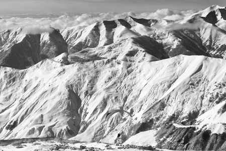 Speed flying at snowy mountains over ski resort at sunny winter day. Caucasus Mountains. Georgia, region Gudauri. Black and white toned landscape.の写真素材