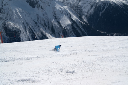 Snowboarder downhill on ski slope in high snowy mountains at sunny winter day. Caucasus Mountains, region Dombay. View from above.の写真素材