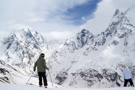 Skier and snowboarder before downhill on off-piste ski slope for freeriding in high snowy mountains at winter day. Caucasus Mountains, region Dombay.の写真素材